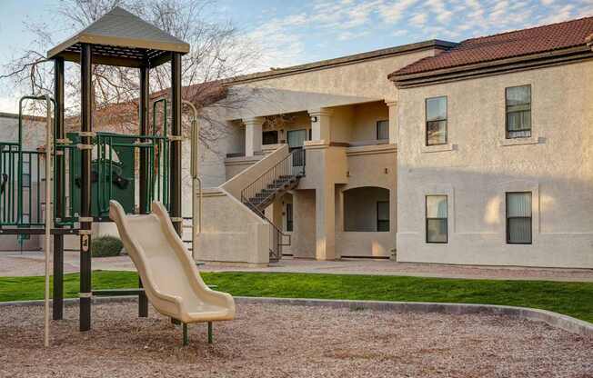 A playground with a slide and a chair in front of a building.