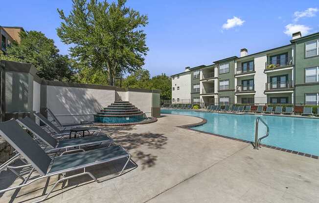 A pool area with sun loungers and a building in the background.