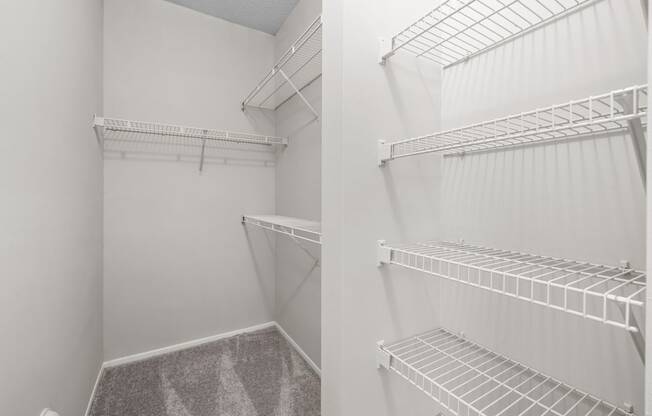 two views of a walk in closet with white walls and shelves