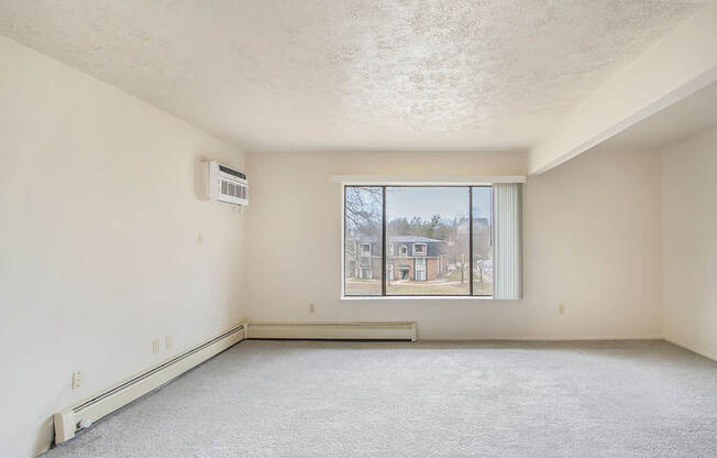 A sparsely furnished room with a window overlooking a residential area.