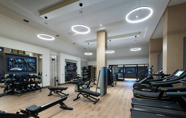 Gym with cardio equipment, weight machines, dumbbells, kettlebells, benches, multiple HDTVs, and wood-style floors