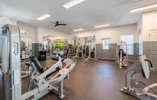 A spacious gym with a variety of equipment including treadmills, weight machines, and a ceiling fan.