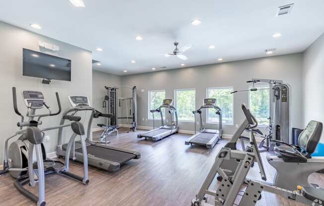 a gym with cardio equipment and a tv