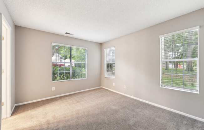 an empty living room with two windows and carpeting