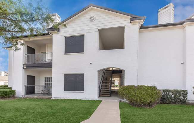 the outlook of a white building with a sidewalk and grass