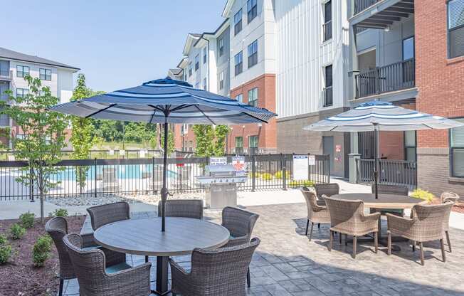 Apartments For Rent In Hermitage, TN - Outdoor Patio Area By The Pool. Patio Has Gas BBQ Grills, Tables With Umbrellas, Chairs, And Maintained Landscaping.