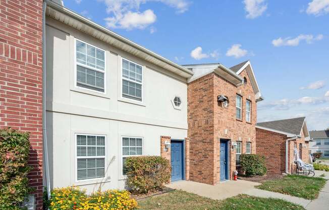A white house with a red brick chimney next to a white house with a blue door.