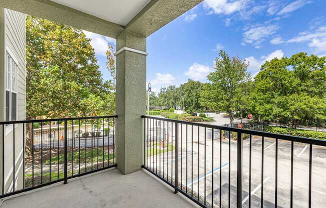 A balcony with a black railing overlooks a parking lot and trees.