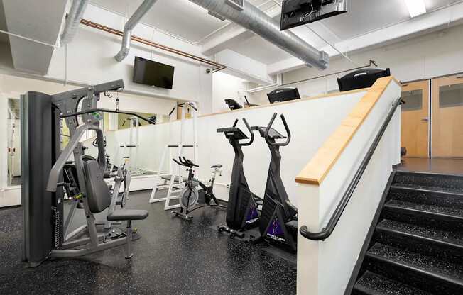 A gym with a variety of equipment including a treadmill, stationary bike, and weight bench.