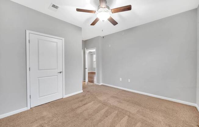 an empty living room with a ceiling fan and a door to a hallway