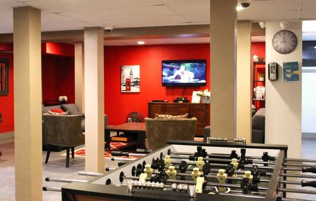 Brookmore apartments rec room with red walls. Features a football table and TV room with couches, console, and coffee table.