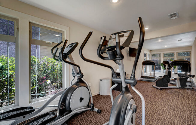 A well-equipped fitness center here at The Bradford with modern cardio machines, including ellipticals and treadmills, arranged in a bright, clean space. Large windows bring in natural light and views of greenery, creating an energizing and comfortable workout environment.