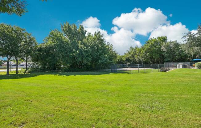 a large grassy field with a tennis court and trees