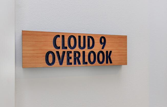 A wooden sign with the text "CLOUD 9 OVERLOOK" in bold, black letters mounted on a light-colored wall.
