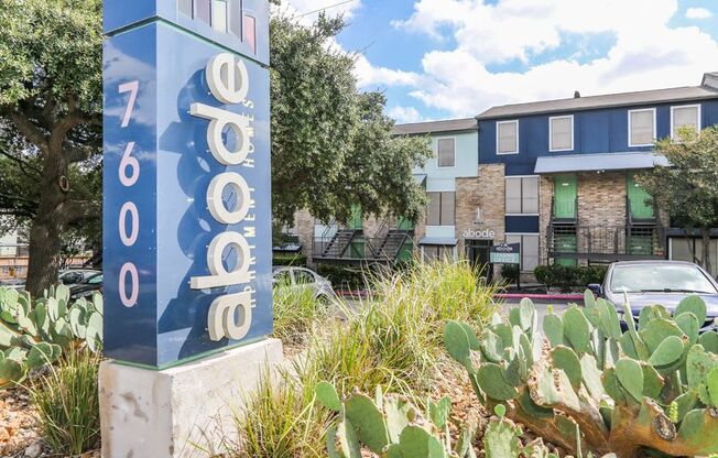 a sign in front of an apartment building with cacti and a parking lot