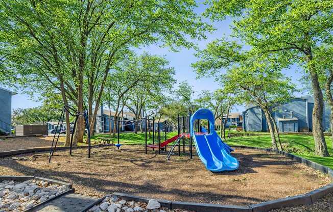 A playground with a blue slide and trees.