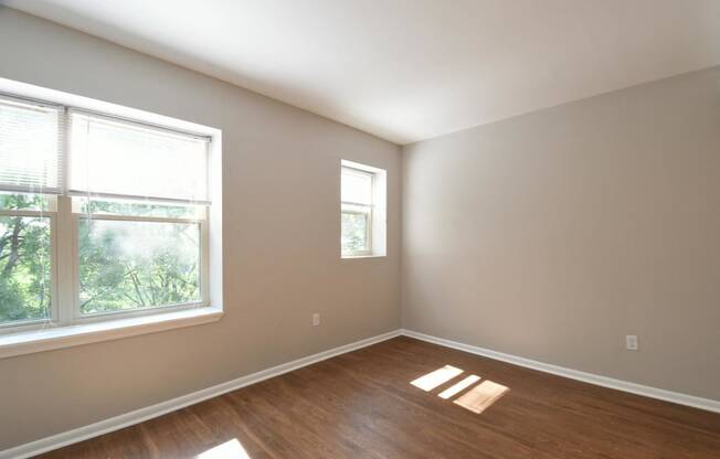 an empty bedroom with a large window and hardwood floors
