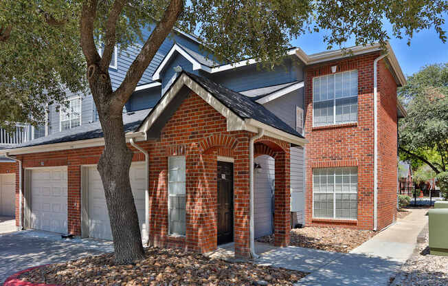 A red brick house with a tree in front.