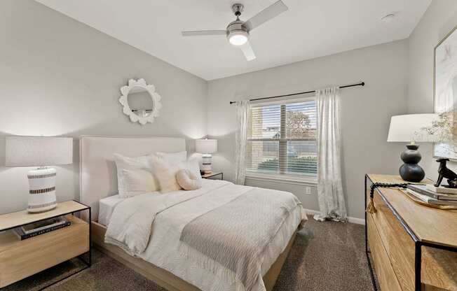 A bedroom with a large bed, a ceiling fan, and a window with white curtains.