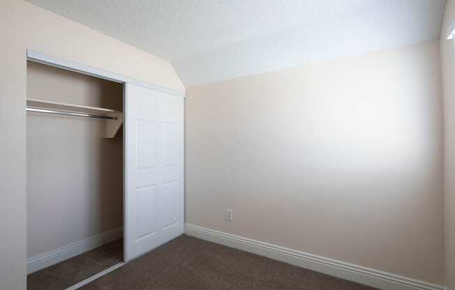 Carpeted bedroom with large closet and window at the Atrium Apartments in San Diego, California.