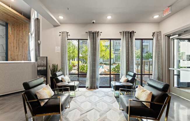 A living room with black leather chairs and a large window with a view of trees.