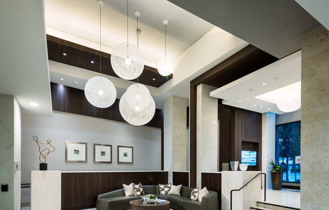 Spacious lobby with high ceilings, a modern globular chandelier, marble floors, a concierge desk, and a curved couch around a coffee table.