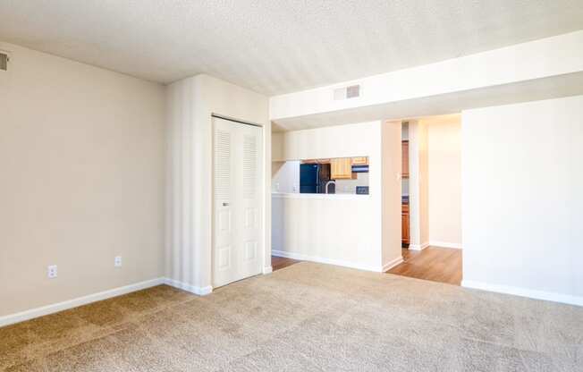 an empty living room with a kitchen in the background