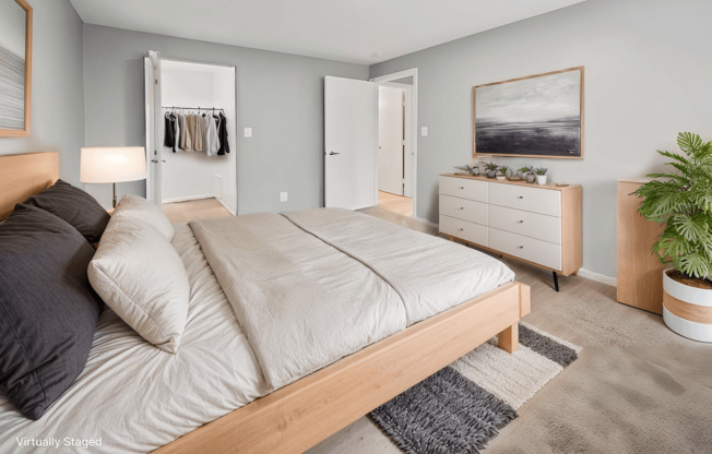 A bedroom with a large bed, a dresser, and a plant.