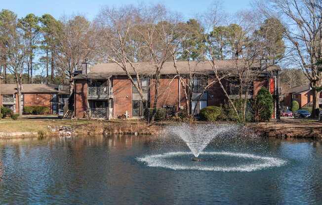 A fountain in the middle of a pond in front of a building.
