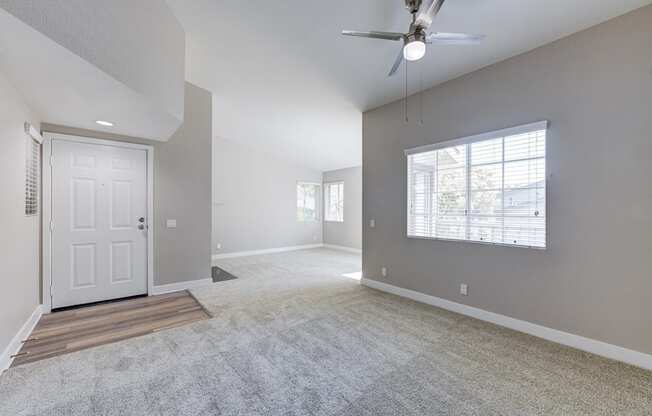 an empty living room with a white door and a ceiling fan