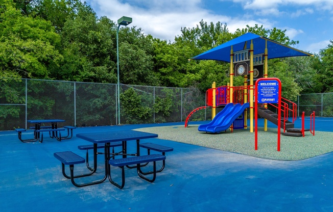 A playground with a blue slide and picnic tables.
