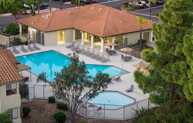 A large outdoor swimming pool surrounded by a fence and lounge chairs.