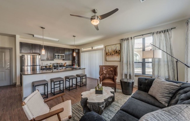 a living room with a couch and a chair in front of a kitchen with a breakfast bar