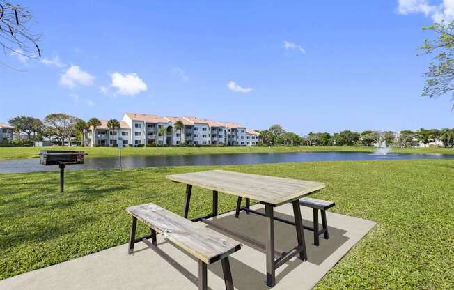 a picnic table in front of a lake with a grill