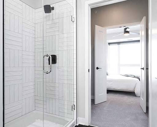 A bathroom with a walk-in shower and a bedroom in the background.