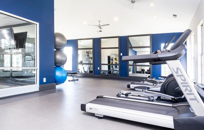 Cardio and strength training equipment in apartment fitness center with blue walls and windows