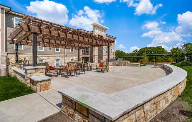 a patio with a stone wall and a wooden pergola