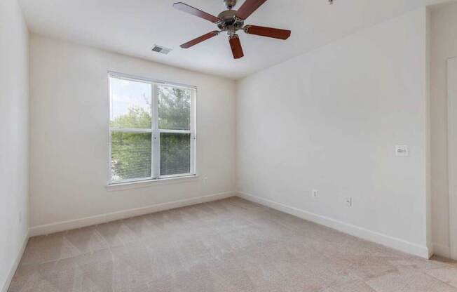 an empty living room with a ceiling fan and a window