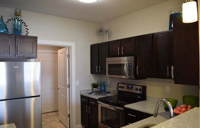 A kitchen with a stainless steel refrigerator and dark brown cabinets.