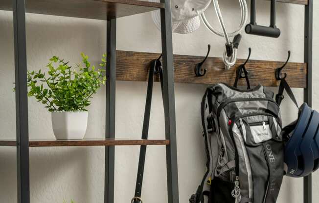 a metal shelving unit with hooks and a backpack on it and plants on the shelves