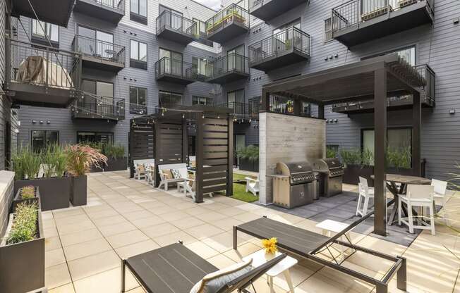 a patio with tables and chairs and a grill in front of an apartment building