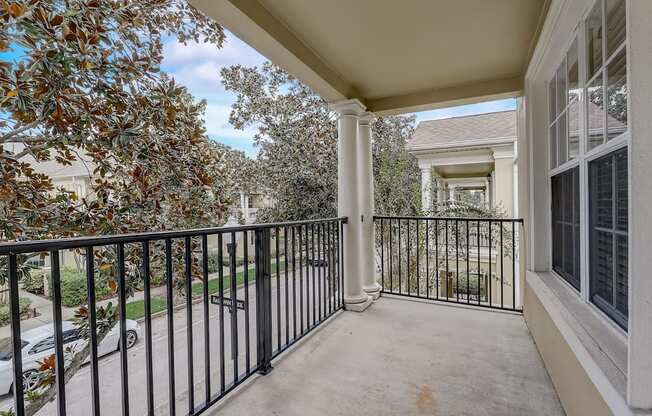 A balcony with a black railing and a view of a tree and a building.