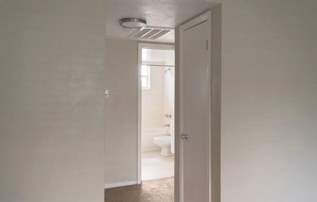 a hallway leading to a white bathroom with a toilet and sink.