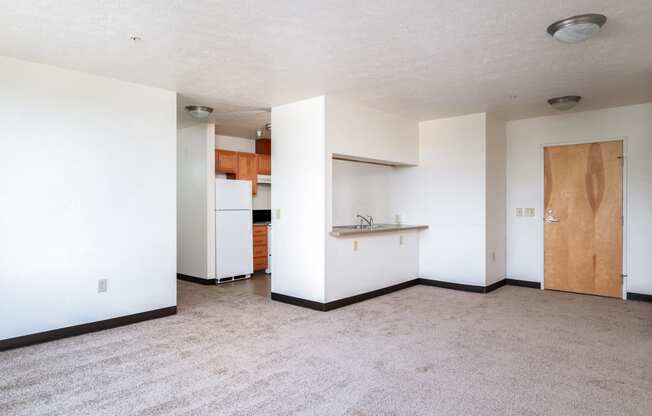 an empty living room and kitchen with a refrigerator and a sink