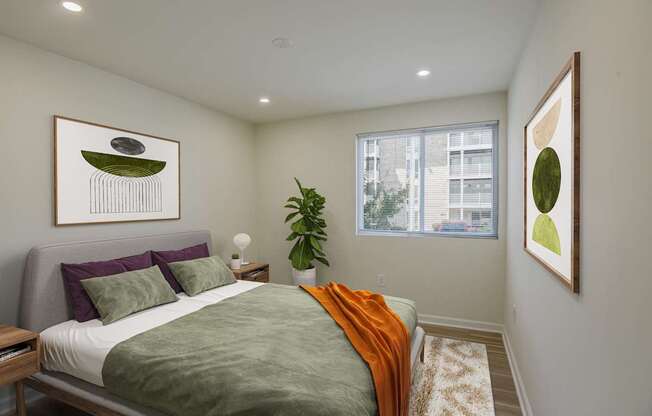 A bedroom with a bed, a potted plant, and two framed pictures on the wall.