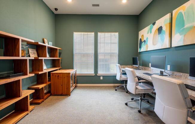 Small room with a book shelf and a long desk with computer monitors and chairs with 2 windows at Mosaic Apartments in Avon, Indiana