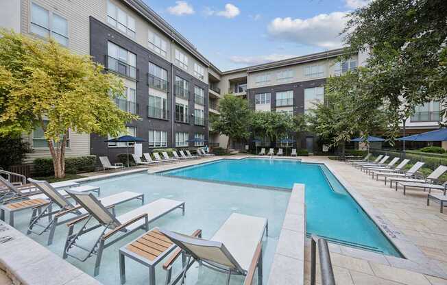 A large swimming pool surrounded by lounge chairs and trees.