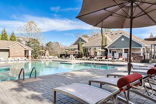 A pool with a bench and an umbrella in front of a house.