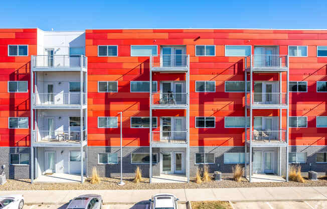 a red apartment building with balconies and cars in front of it