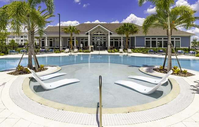 a large swimming pool with white chairs and a building in the background